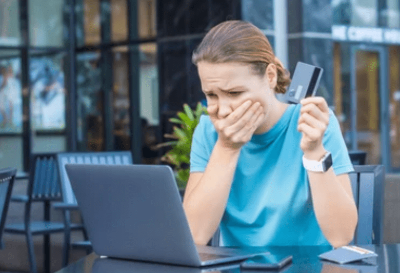 Woman with hand over mouth and credit card in hand looking at her laptop